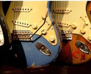 A row of electric guitars with a vintage look, featuring worn paint and visible dings. Each guitar is a different color, including blue and brown, and has a distinct retro design.