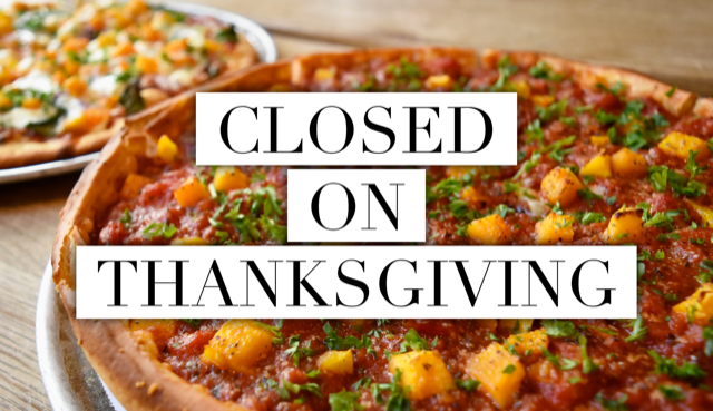 Close-up of two pizzas on a wooden table. A prominent sign reads CLOSED ON THANKSGIVING in bold letters, overlaying the image. The front pizza is topped with herbs and diced vegetables.